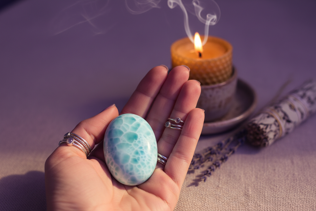 Polished Larimar crystal held in an open palm with candle, lavender, and soft smoke in the background — calming crystal for anxiety, boho metaphysical wellness